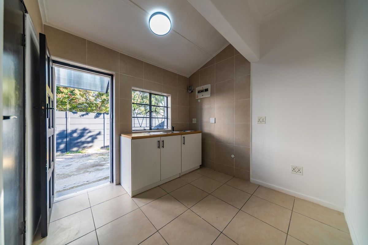 A clean and functional laundry area featuring tiled flooring, built-in base cabinetry with a sink, and direct access to the exterior.