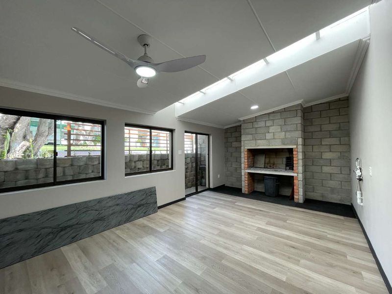 Spacious enclosed patio featuring a built-in braai, modern laminate flooring, a ceiling fan, and a large skylight for natural light.