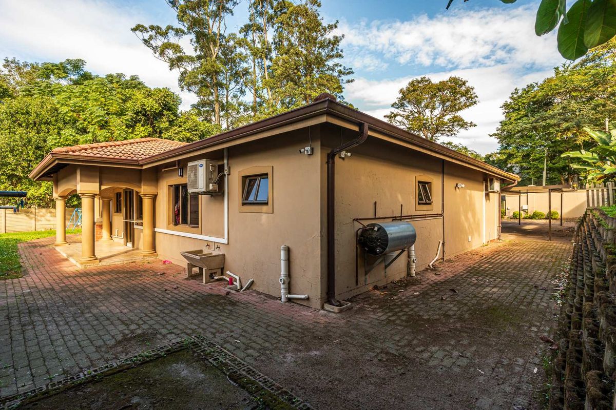Rear exterior view of the house featuring a covered patio with columns, paved courtyard area, and exterior utility installations.