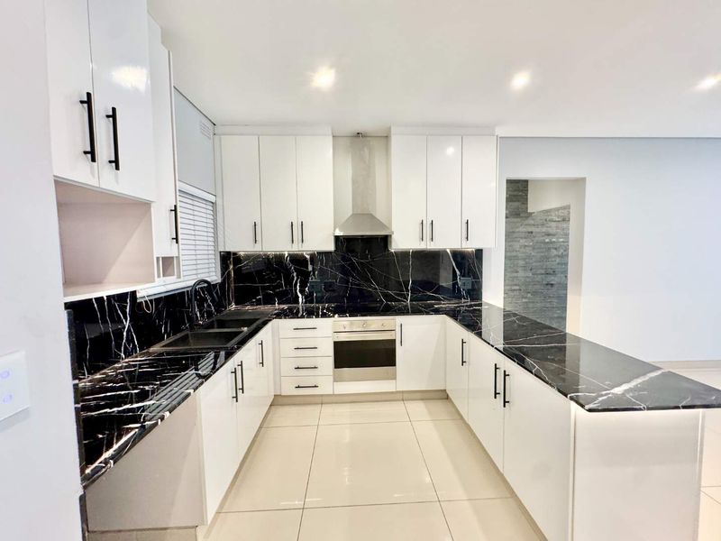 Modern kitchen featuring high-gloss white cabinetry, striking black marble-look countertops and splashback, stainless steel appliances, and sleek tiled flooring.