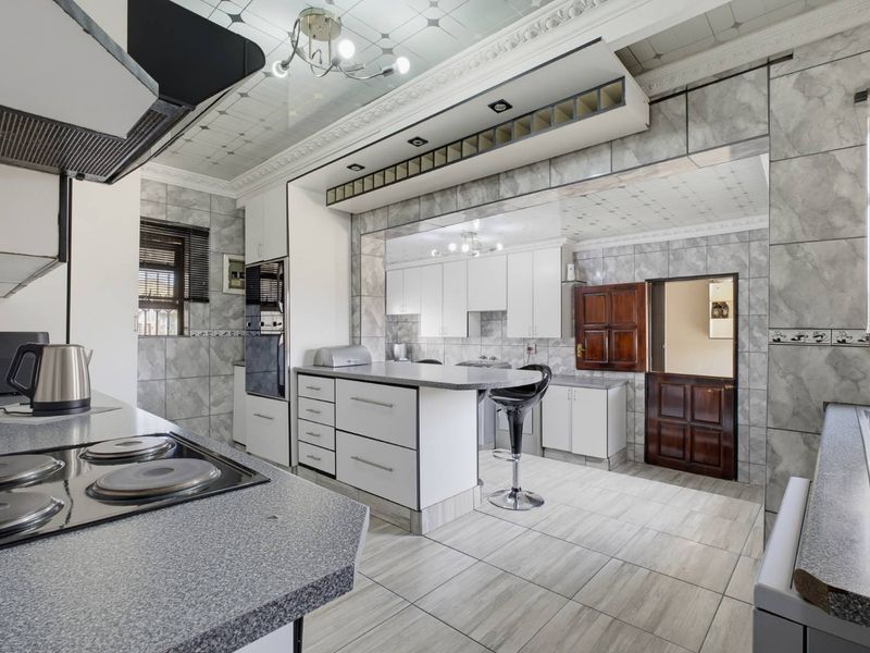 Spacious kitchen featuring extensive built-in cabinetry, a central island, electric hob, extractor fan, and tiled finishes throughout.