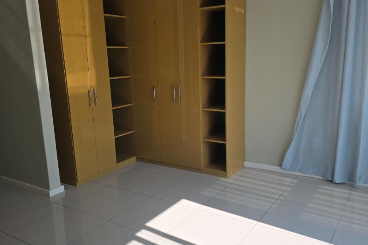 A bright, empty bedroom featuring modern built-in cupboards, neutral wall paint, and clean tiled flooring throughout.