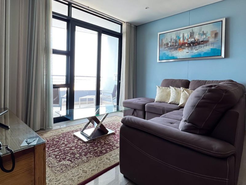 A bright living room featuring large sliding glass doors that open onto a balcony, complemented by neutral tiled flooring and recessed lighting.