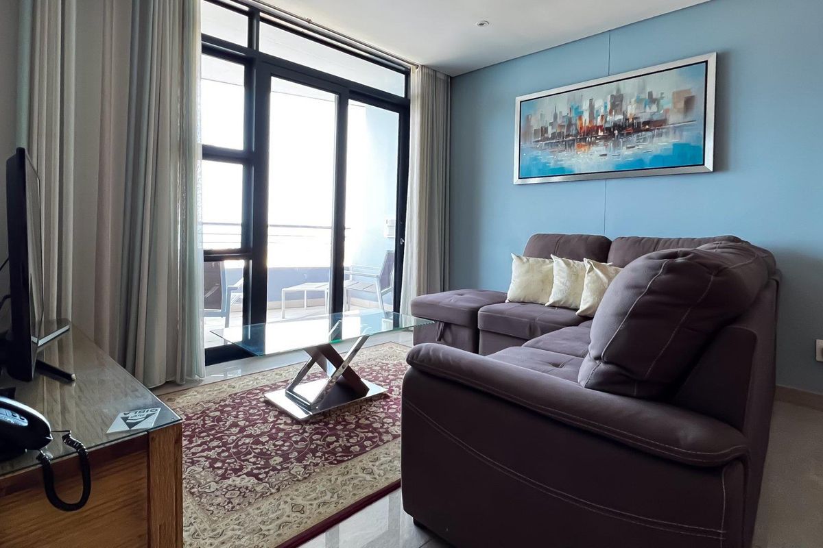 A bright living room featuring large sliding glass doors that open onto a balcony, complemented by neutral tiled flooring and recessed lighting.