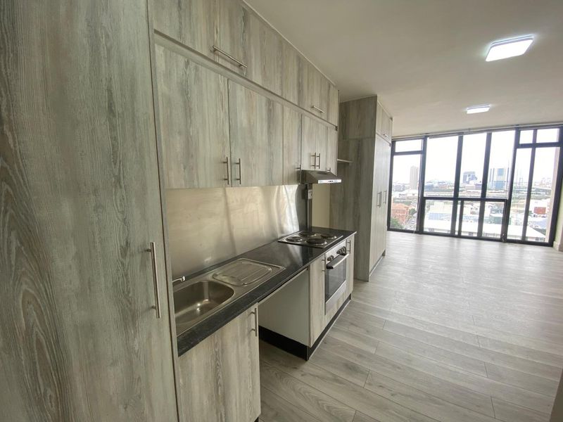 Modern open-plan kitchen featuring wood-grain cabinetry, integrated appliances, and floor-to-ceiling windows with expansive city views.