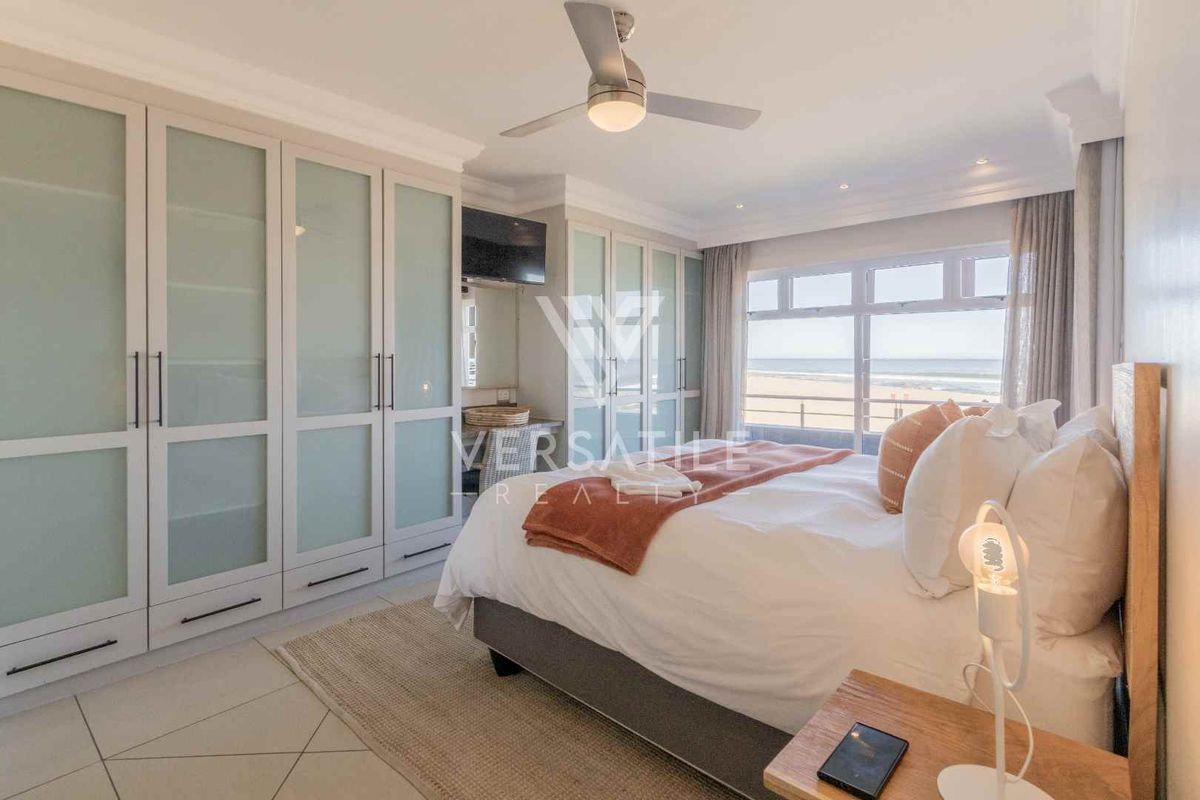 A well-appointed bedroom featuring extensive built-in cabinetry, a ceiling fan, and large windows offering direct ocean views.