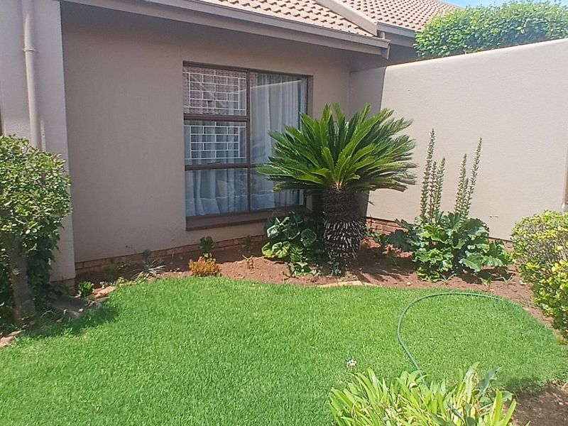 A well-maintained rear garden area featuring a manicured lawn, established shrubs, and a private boundary wall adjacent to the townhouse structure.