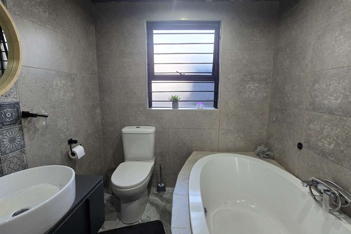 Modern bathroom featuring a built-in bathtub, vessel sink with vanity, and neutral grey wall and floor tiling.