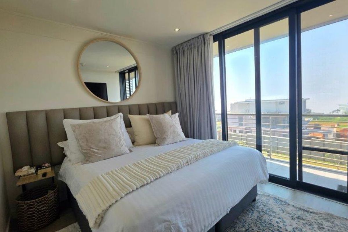 A well-maintained bedroom featuring a large upholstered headboard, recessed lighting, and floor-to-ceiling sliding glass doors providing access to a balcony.