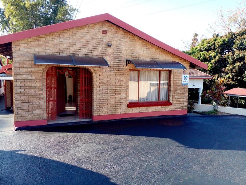 Front exterior view of a face brick house featuring a paved driveway, security gate, and protective window awnings.
