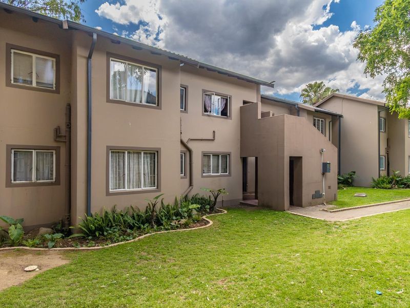 A view of the rear apartment building facade featuring a paved walkway, landscaped garden area, and exterior building finishes.