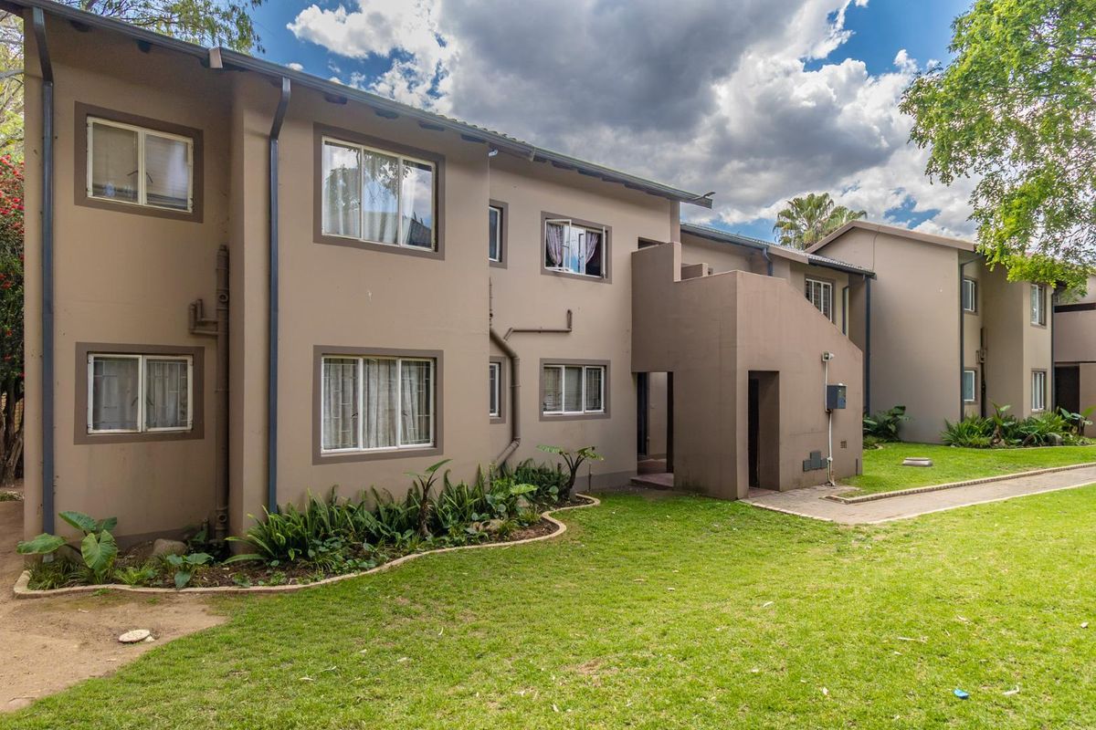 A view of the rear apartment building facade featuring a paved walkway, landscaped garden area, and exterior building finishes.