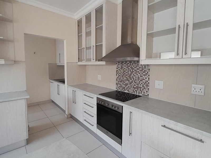 Modern kitchen featuring light wood-grain cabinetry, glass-fronted display units, integrated electric oven and hob, and a mosaic tile splashback with neutral tiled flooring.