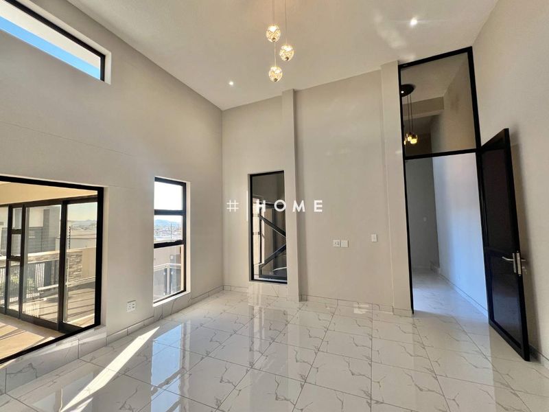 A bright, modern living area featuring high ceilings, large windows with aluminium frames, and polished porcelain tile flooring.