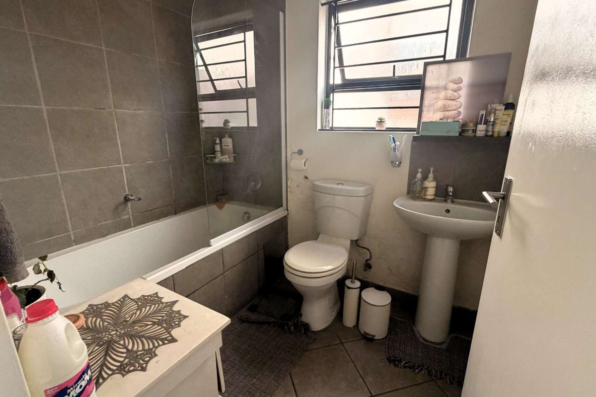 A functional bathroom featuring a bathtub with a glass screen, pedestal basin, and toilet, finished with neutral wall and floor tiling.