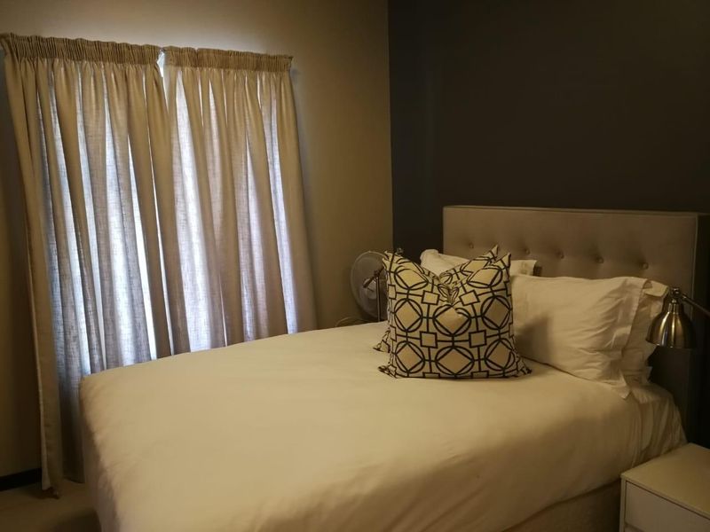 A comfortable bedroom featuring a neutral color palette, an accent wall, and floor-to-ceiling curtains providing natural light control.