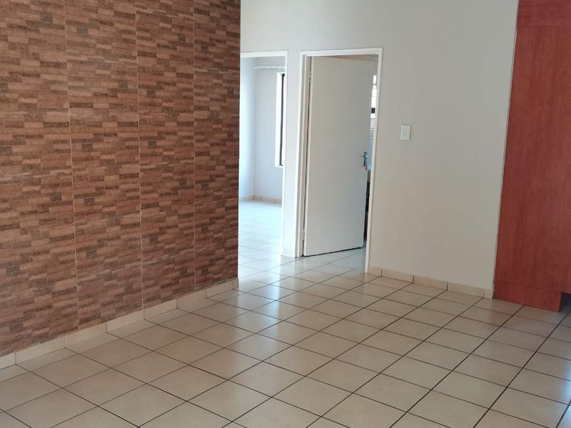 An empty living area featuring tiled flooring, a textured feature wall, and a built-in cupboard, leading to an adjacent room.