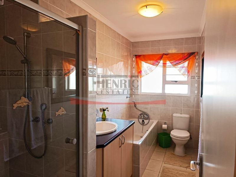 A functional bathroom featuring a shower enclosure, built-in vanity with basin, bathtub, and toilet, finished with neutral wall and floor tiling.