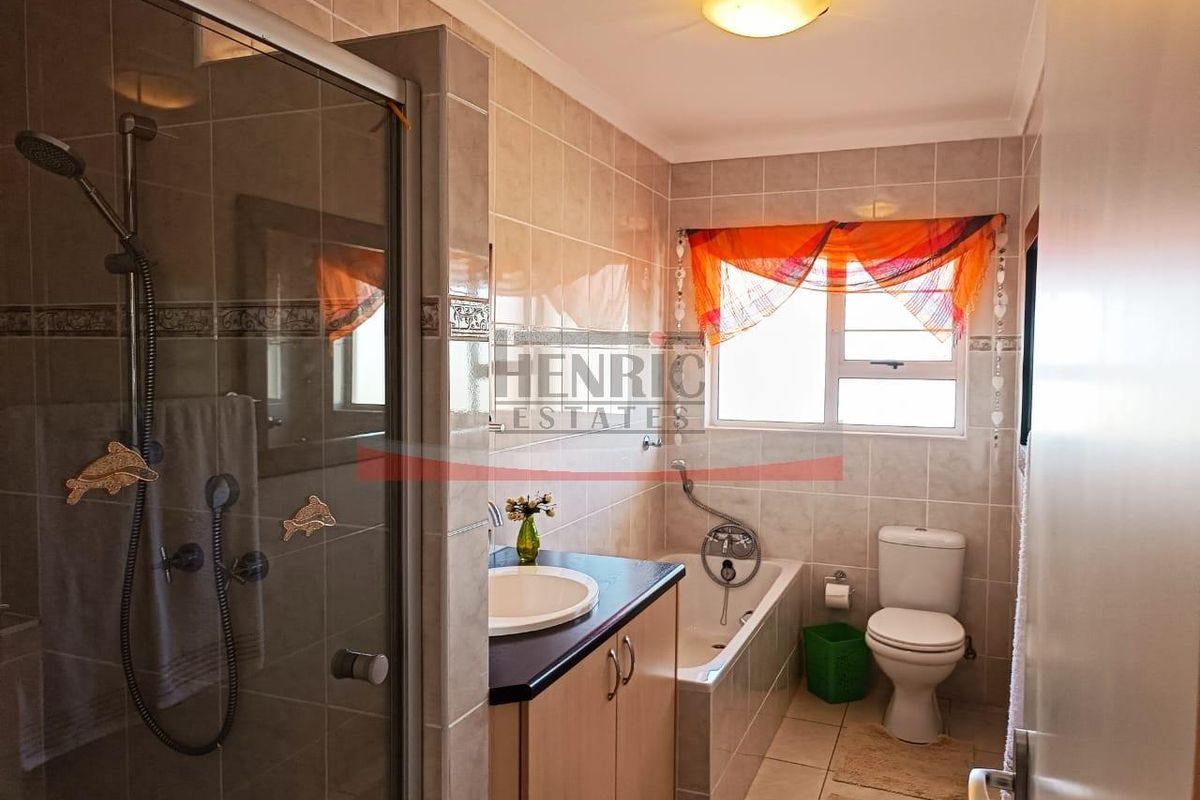 A functional bathroom featuring a shower enclosure, built-in vanity with basin, bathtub, and toilet, finished with neutral wall and floor tiling.
