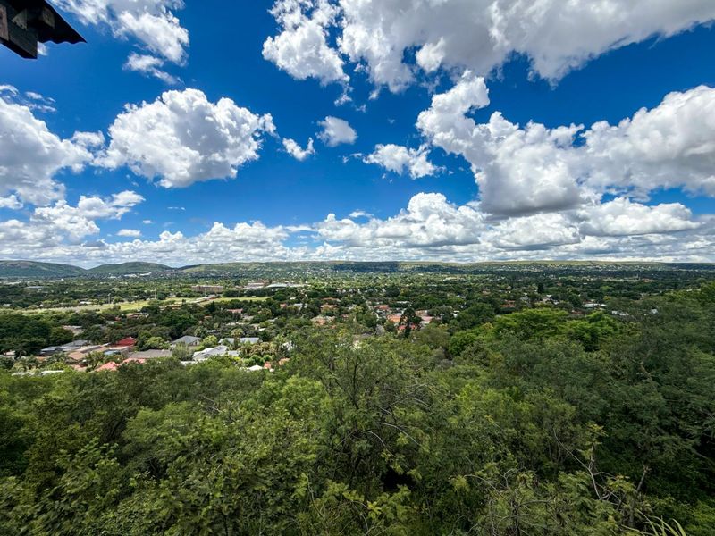 An expansive elevated view overlooking a lush green suburban landscape with distant hills under a bright blue sky.