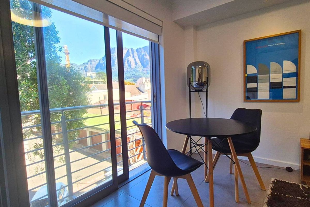 A bright living area featuring large sliding glass doors that open to a balcony with mountain views and modern tiled flooring.