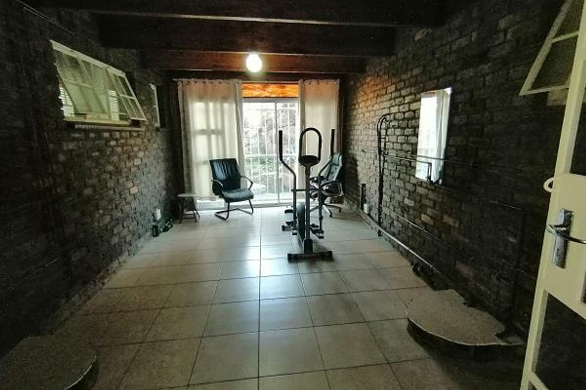 A rustic living space featuring exposed brick walls, timber ceiling beams, and tiled flooring, with access to an outdoor area via sliding glass doors.