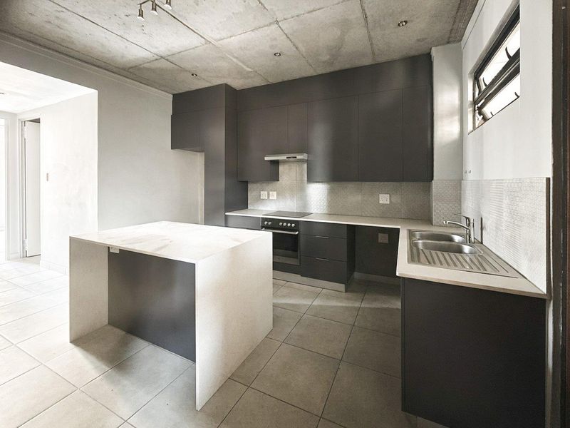 Modern kitchen featuring dark cabinetry, stone countertops, a central island, and an exposed concrete ceiling, offering a sleek and contemporary aesthetic.