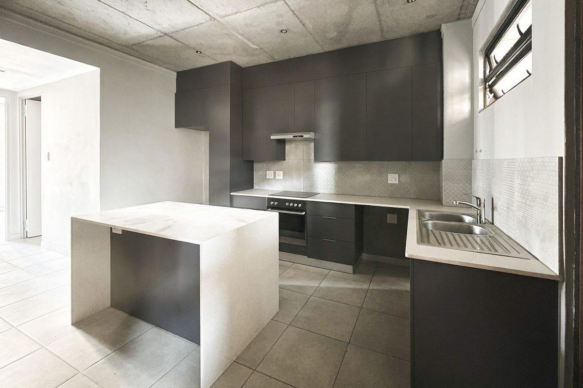 Modern kitchen featuring dark cabinetry, stone countertops, a central island, and an exposed concrete ceiling, offering a sleek and contemporary aesthetic.