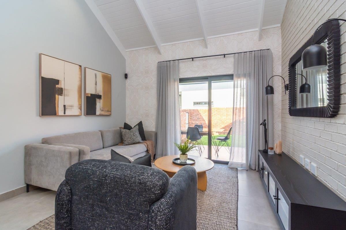 A bright living room featuring a vaulted ceiling with exposed beams, a textured brick feature wall, and sliding glass doors leading to the patio.