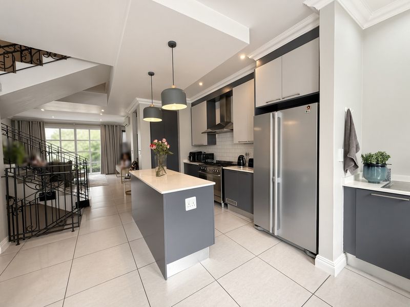 Modern open-plan kitchen featuring a central island, sleek cabinetry, quartz countertops, and a stylish wrought iron staircase leading to the upper level.