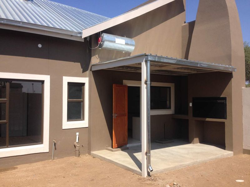 Rear exterior view featuring a covered patio with a built-in braai, solar geyser installation, and concrete flooring.
