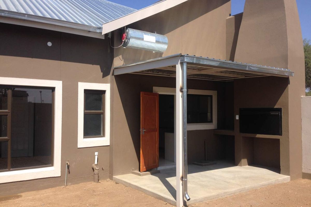Rear exterior view featuring a covered patio with a built-in braai, solar geyser installation, and concrete flooring.