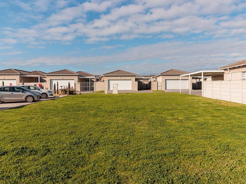 A view of a residential townhouse complex featuring multiple units with tiled roofs, garage doors, and a shared paved driveway area.