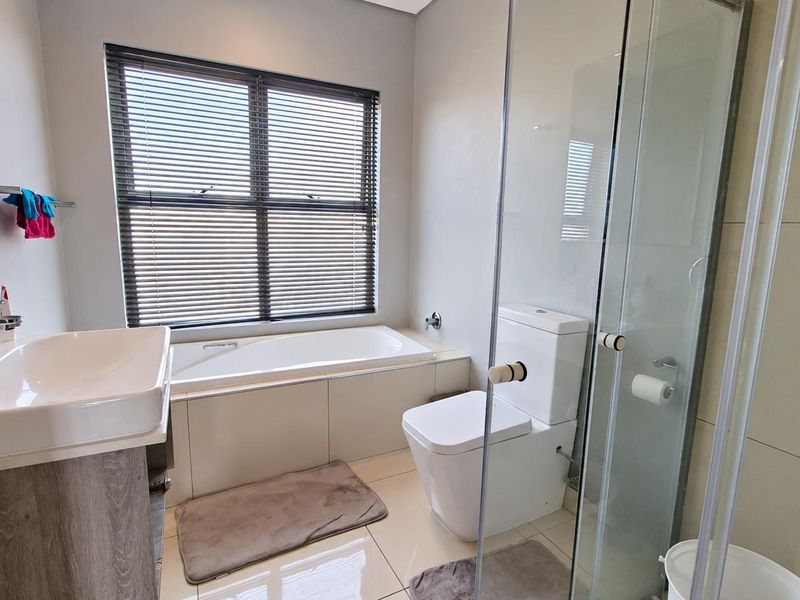 Modern bathroom featuring a built-in bathtub, separate glass-enclosed shower, wall-mounted toilet, and a vanity basin with neutral tiled finishes.