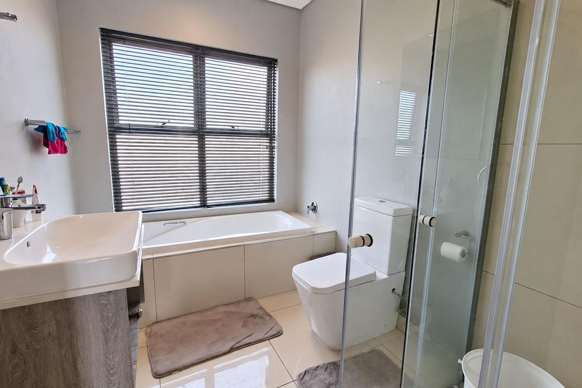 Modern bathroom featuring a built-in bathtub, separate glass-enclosed shower, wall-mounted toilet, and a vanity basin with neutral tiled finishes.