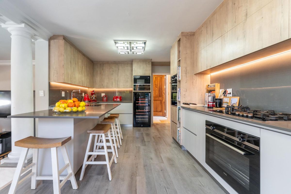 Modern kitchen featuring light wood cabinetry, stone countertops, integrated appliances, a central island, and sleek under-cabinet lighting.