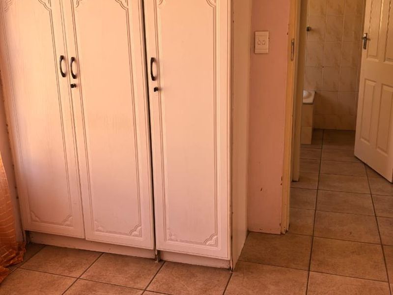 A bedroom featuring built-in cupboards and tiled flooring, with an adjacent bathroom visible through the doorway.