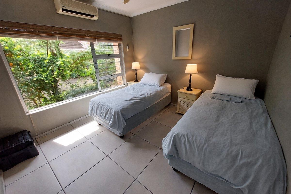 A bedroom featuring tiled flooring, a large window with garden views, and a wall-mounted split-system air conditioner.