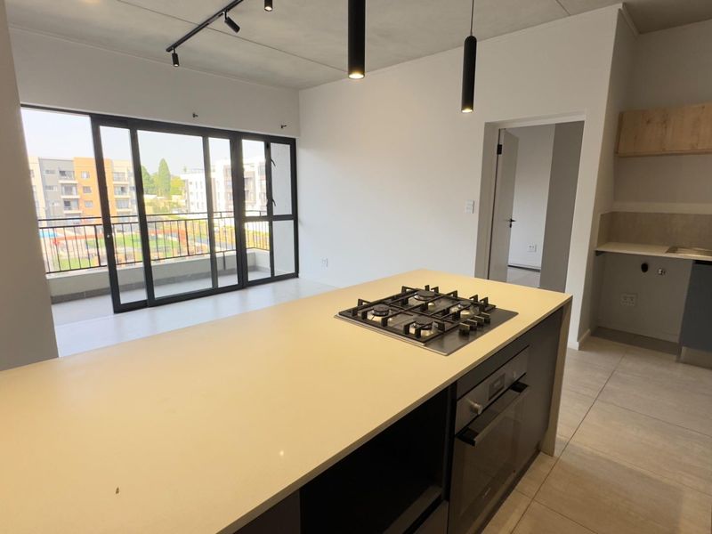 Modern open-plan kitchen and living area featuring a central island with gas cooktop, sleek cabinetry, and large sliding doors leading to a balcony.