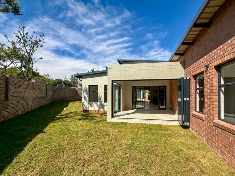 Rear view of the property featuring a manicured lawn, a covered patio with stacking doors, and a combination of brick and rendered wall finishes.