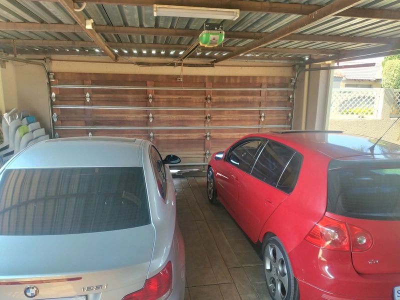 A functional double garage featuring a sectional timber door, tiled flooring, and an exposed steel roof structure with an automated door motor.