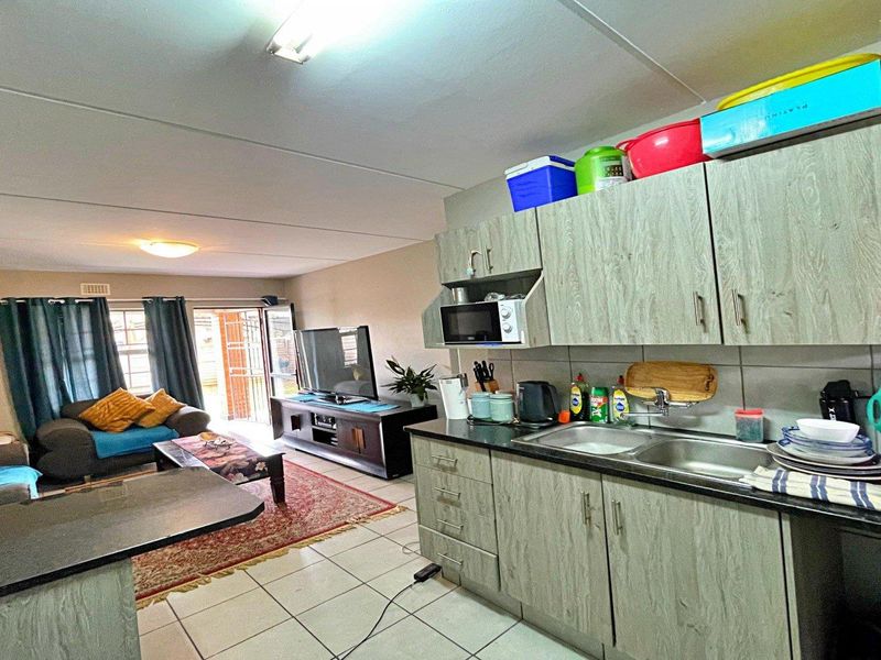 Open-plan living area featuring a functional kitchen with built-in cabinetry, laminate countertops, and tiled flooring, flowing into a comfortable lounge space.