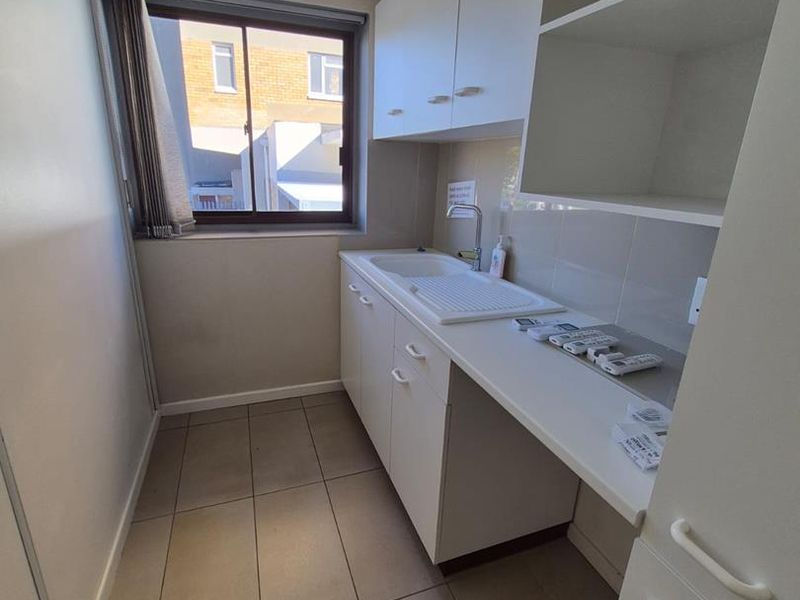 A clean and functional scullery or utility area featuring built-in white cabinetry, a sink, and tiled flooring with ample storage shelving.