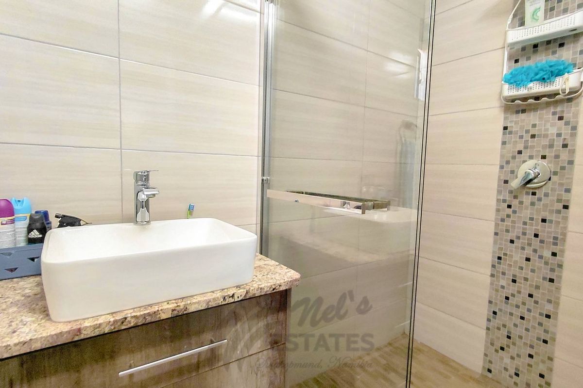 Modern bathroom featuring a vessel sink on a granite vanity top and a glass-enclosed shower with mosaic tile accents.