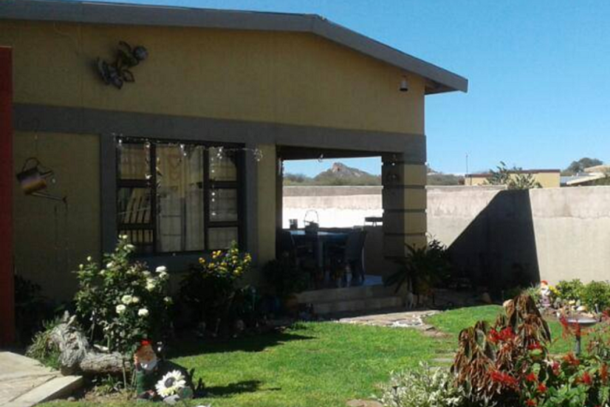 A view of the rear exterior of the house featuring a covered patio area, landscaped garden, and perimeter boundary wall.