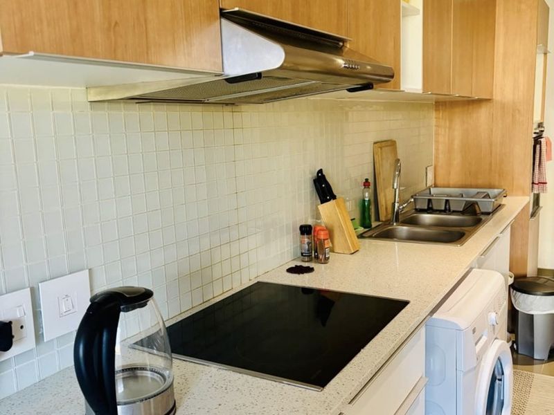 Modern kitchen featuring light wood cabinetry, stone countertops, a tiled backsplash, integrated hob, extractor fan, and a built-in washing machine.