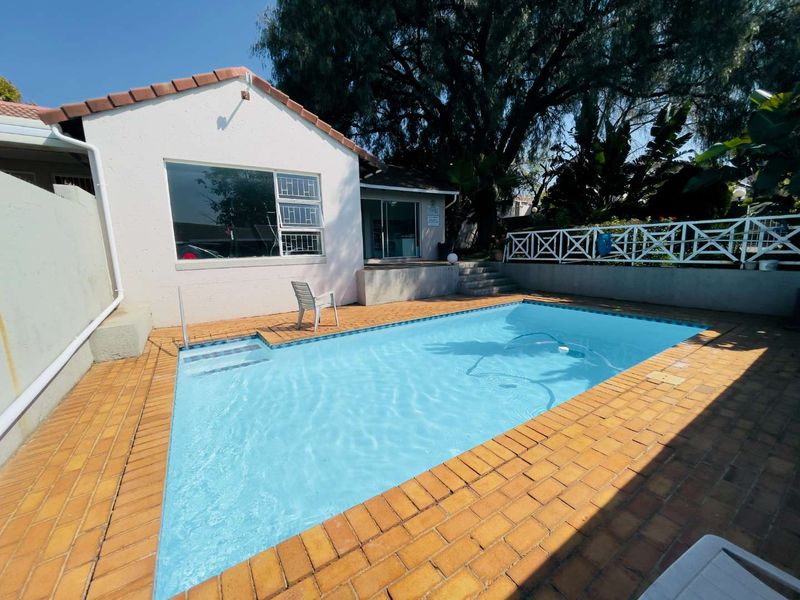 Outdoor pool area featuring a swimming pool, brick paving, and a concrete retaining wall with a white lattice fence.
