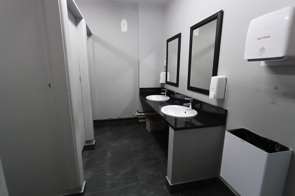 A functional office bathroom featuring a dual vanity with granite countertops, tiled flooring, and multiple toilet cubicles.