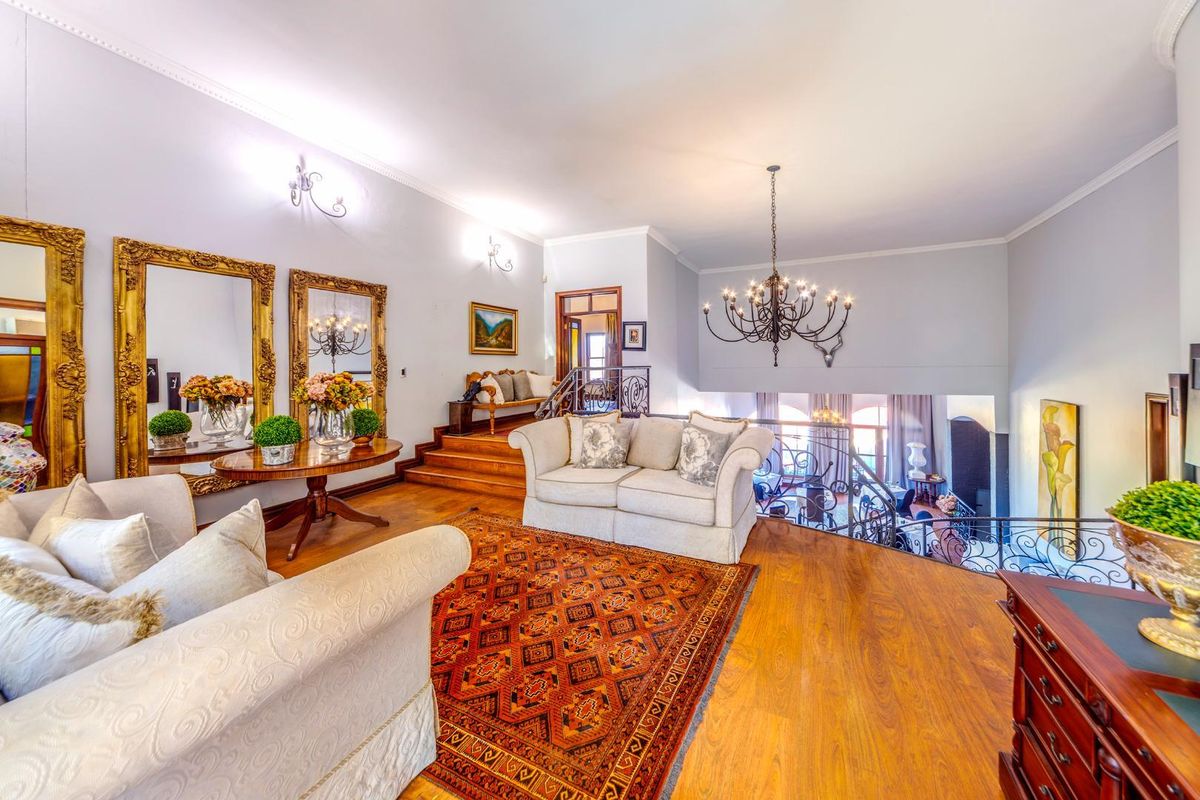 Spacious living area featuring warm wood flooring, a decorative chandelier, and an open-plan layout overlooking the lower level with elegant wrought-iron railings.