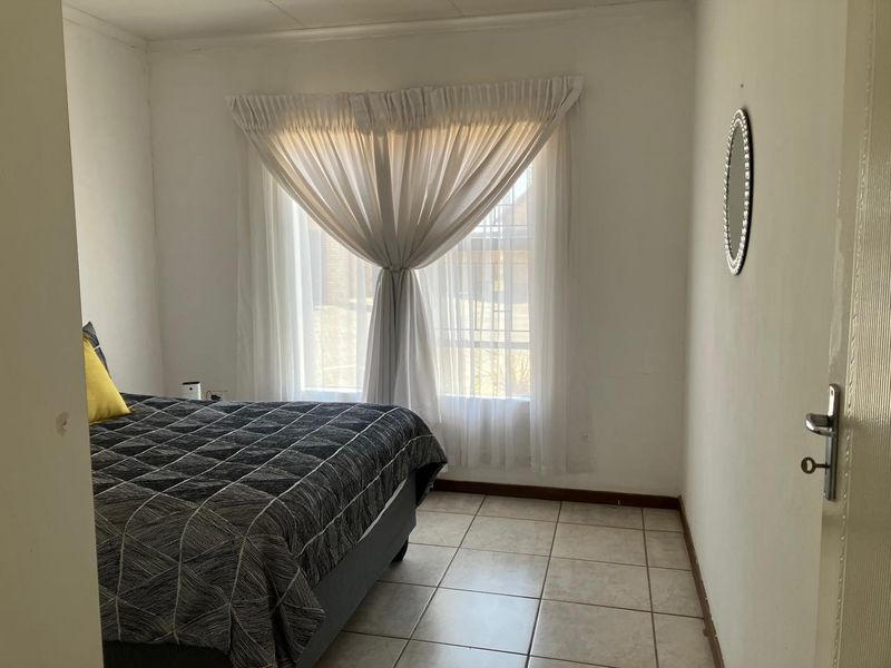 A functional bedroom featuring tiled flooring and a window with curtains, offering a neutral space ready for personalization.